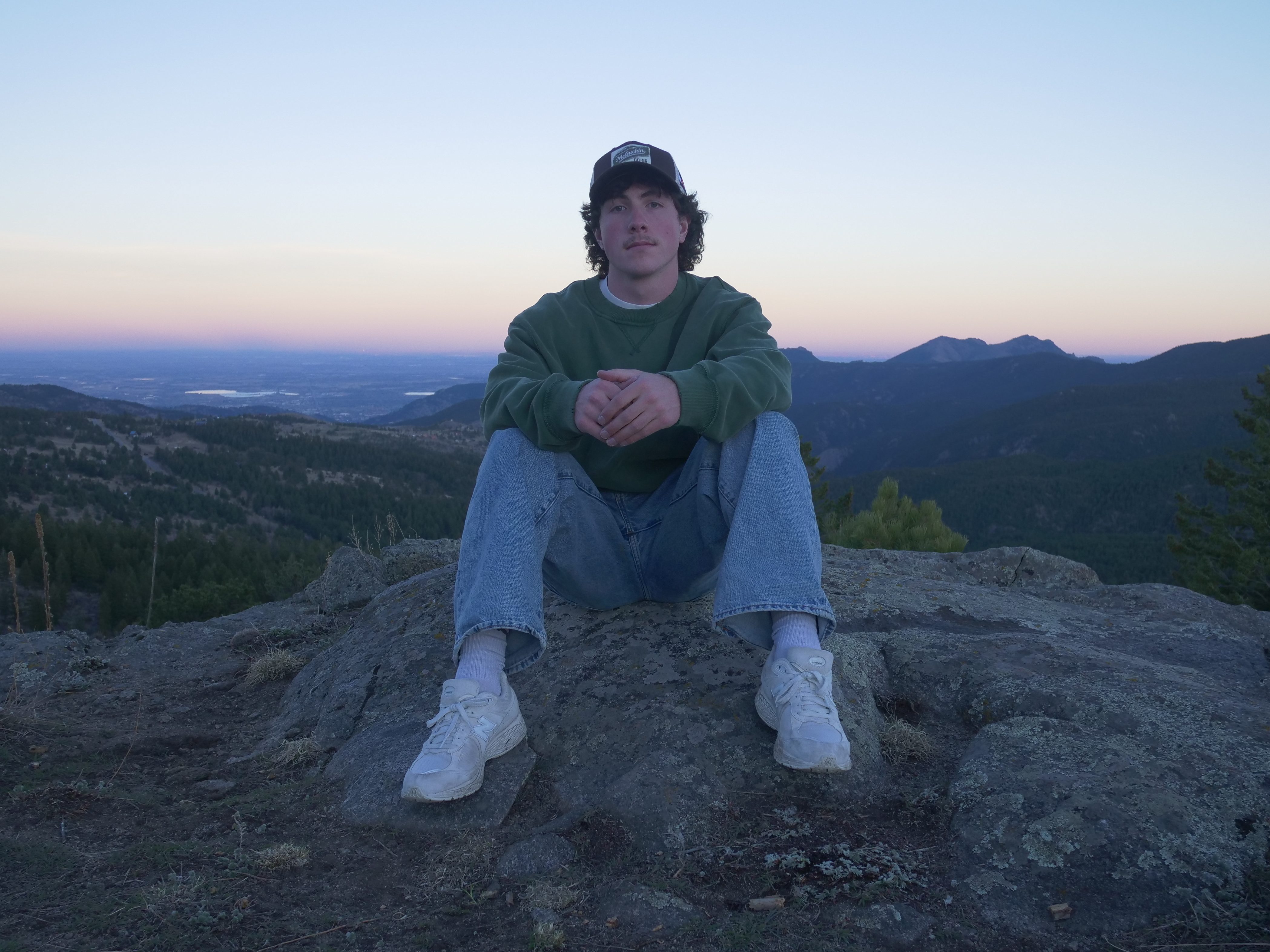 Songwriter Logan Proffitt sitting on a mountain overlooking Boulder, Colorado at sunset. 